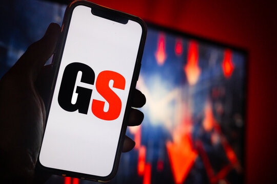 Hand Holding Phone with Gamestop (GME) Logo and Monitor in the Background Showing Red Arrows Pointing Down Suggesting Stock Decline