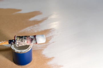 Top view of a can of white paint with a brush on it. The background is a wooden board that has...
