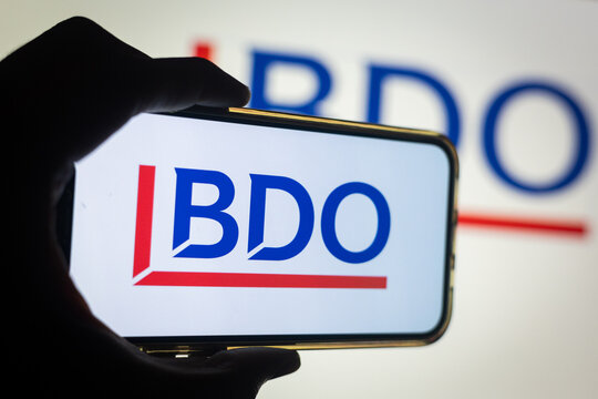 Silhouette of Hand Holding Phone with BDO (BDO) Logo in Front of Computer Screen Displaying BDO Accounting and Financial Services Logo