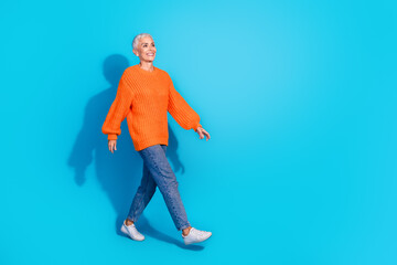 Photo of positive old lady walking look empty space wearing pullover denim jeans isolated blue color background