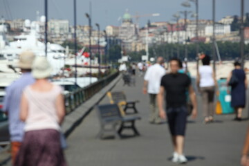 Tourists walking on a quay in blur near luxury yachts and cityscape