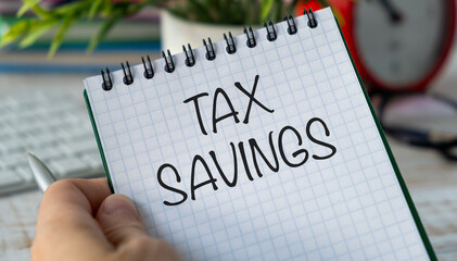 A person is holding a spiral notebook with the word Tax Savings written on it