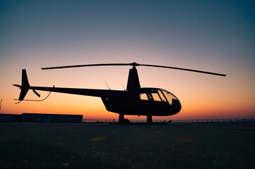 A black helicopter is sitting on the ground at sunset.