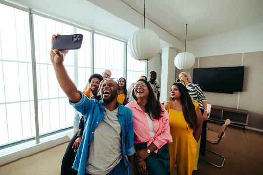 Energetic team from an advertising agency taking a fun group selfie in a modern office.