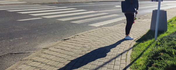 A person standing on a sidewalk near a crosswalk, with a shadow cast on the ground, creating a contrast between light and shadow. Ideal for urban lifestyle themes.