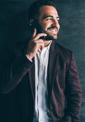 Cheerful caucasian male in trendy formal wear looking away talking on mobile phone enjoy good connection, smiling prosperous businessman making cellular call standing near black wall indoors