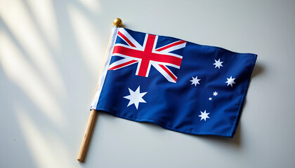 Australian flag displayed on a wooden stick against a neutral background in bright daylight