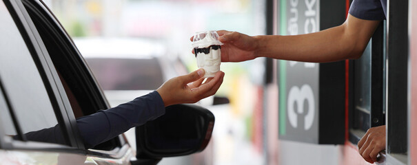 Hand Man in car receiving coffee in drive thru fast food restaurant. Staff serving takeaway order for driver in delivery window. Drive through and takeaway for buy fast food for protect covid19.