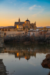 Fototapeta premium Scenic view of the historic Puente Romano and La Mezquita Cathedral in the background in Cordoba, Andalusia, Spain in golden hour at sunset. Roman Bridge on Guadalquivir river and The Great Mosque.