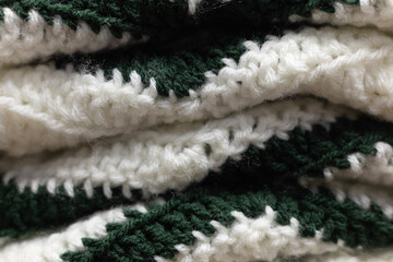 close-up of folded green zigzag blanket with white and hunter green accents, crocheted or knitted,...