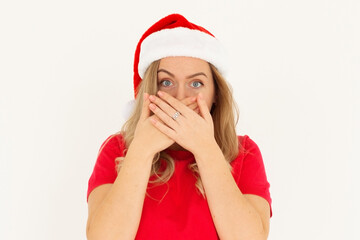 Merry shocked amazed young woman wear red xmas t-shirt Santa hat posing cover mouth with hand isolated on white background. Happy New Year 2025 holiday concept