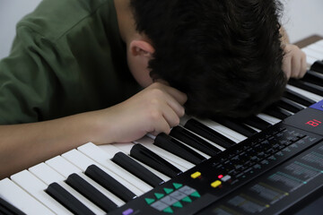 Angry boy with his electric keyboard classes. Preteen frustrated with his music lesson. Concept of excessive homework and studies.