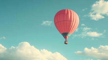 Fototapeta premium A red hot air balloon floats against a clear blue sky with white clouds.
