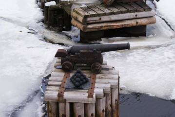Historical cannon with cannonballs on the bank of a frozen river. Ice covered with snow. Winter. Nature.