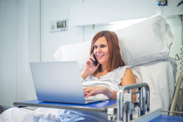 Woman on hospital bed talking on phone, engaged in conversation with laptop nearby