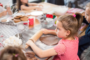Children baking festive treats, rolling cookie dough