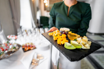 waiter presenting a tray of assorted fruit pieces and a dipping sauce at an elegant event. tray includes strawberries, kiwi, and pineapple, arranged beautifully for a sophisticated dining experience.