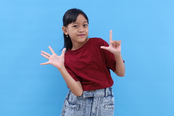Happy asian little girl standing while showing seven fingers. Isolated on blue