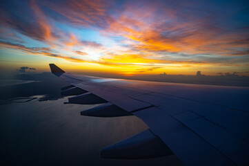plane wing is flying over the ocean with a beautiful sunset in the background