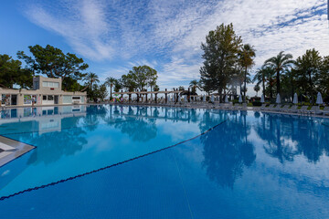 Magnificent view, swimming pool with blue sky with clouds. Holiday hotel in Antalya. Great relaxation and peaceful atmosphere, palm trees, sun loungers reflections.