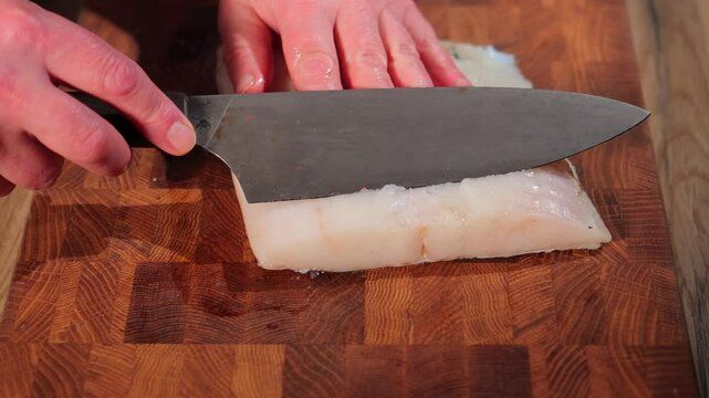 Male hands cutting white fish on a wooden board