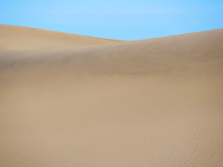 Sand textured pattern with copy space close up in Maspalomas, Gran Canaria. Abstract background wallpaper. Sand waves in a desert dune against the sky