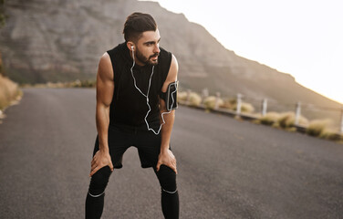 Man, tired and recovery for outdoor workout, exercise and wellness as fitness routine in road. Male person, athlete and earphones for music, health and cardio in rest or break for training or sports