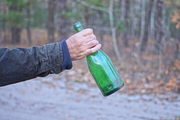 one hand of a man holding a large green dirty glass bottle on the street