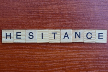  the gray word hesitance of gray small wooden letters lie on a brown table