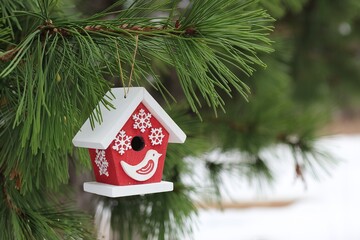 A red and white wooden birdhouse ornament hanging on a pine tree branch with green needles