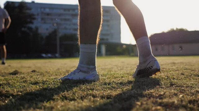 Male feet of professional footballers passing soccer ball on stadium at sunset. Legs of sportsmen kicking ball at green field. Young men training at meadow. Concept of a freestyle football. Slow mo