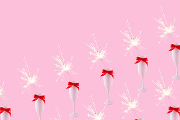 A champagne glass with red bow and sparkler on a pastel pink background. Celebration event concept. Copy space.