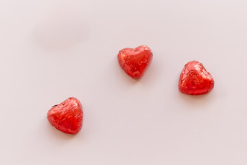 Three heart-shaped candies in red wrappers on a pink background, sweets for Valentine's Day, love...