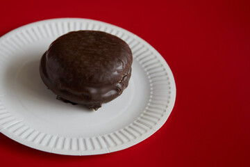 Choco Pie confection, covered with icing, on a white disposable paper plate on a red background, chocolate dessert.