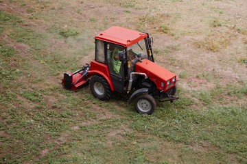 Grass clearing by the tractor with a mower on a picturesque field.