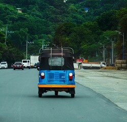 Tuk Tuk jedzie w stronę jungli. Niebieska autoriksza, szeroka droga i jungla. Tuk tuk car na Filipinach. © Adam