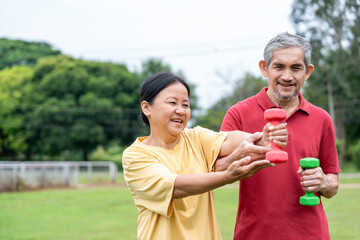 Naklejka premium asian senior married couple doing exercise in the nature park together,elderly man support a wife to workout with dumbbell