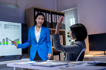 Two businesswomen discussing and brainstorming using data on a monitor in the office at night