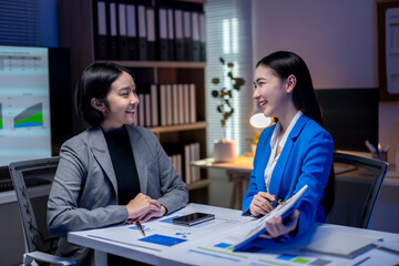 Two businesswomen having a productive meeting discussing financial charts in the office at night