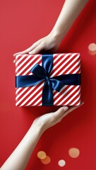 Obraz premium Female hands holding gift box on red bokeh background, top view. Copy space valentine, mother's day, birthday theme. Gift box with ribbon bow