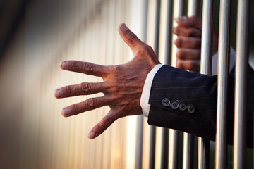 Hand Reaching Through Prison Bars in Formal Attire