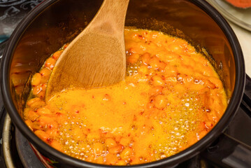 Stir the boiling sea buckthorn berries with sugar in a saucepan with a wooden spoon.