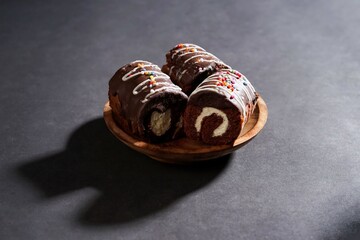 Chocolate roll cake with fresh cream in wooden plate isolated on dark background. chocolate swiss roll cake.