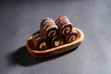 Chocolate roll cake with fresh cream in wooden plate isolated on dark background. chocolate swiss roll cake.