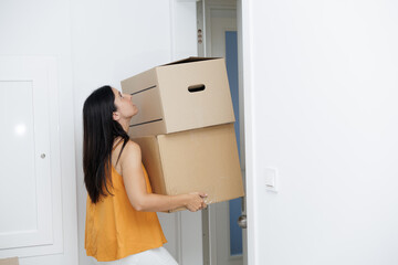Young woman arriving home with moving boxes. She carries two heavy boxes and walks through the door. Real estate, mortgage, new life.