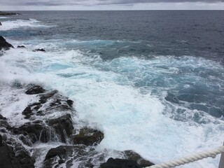 Powerful ocean waves crash against the rugged rocky shore, creating a dramatic seascape under a...