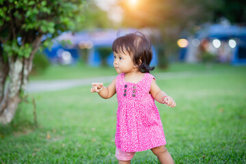 Baby girl walking outdoors dressed in pink stripped dress. Happy kid. Happy childhood.