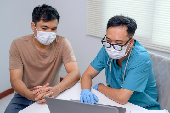 A male Asian doctor wearing a mask uses a laptop computer during an outbreak to discuss treatment plans