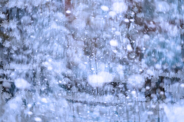 Winter landscape through a frozen window. Blurred snow background. Trees and plants covered with snow.