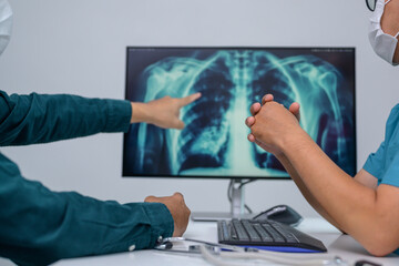 A close-up picture of a doctor showing chest x-ray result in hospital talking to patient and male doctor explaining chest x-ray on computer screen